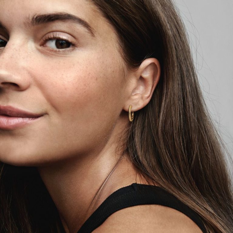 Person wearing a small gold hoop earring with a textured design.