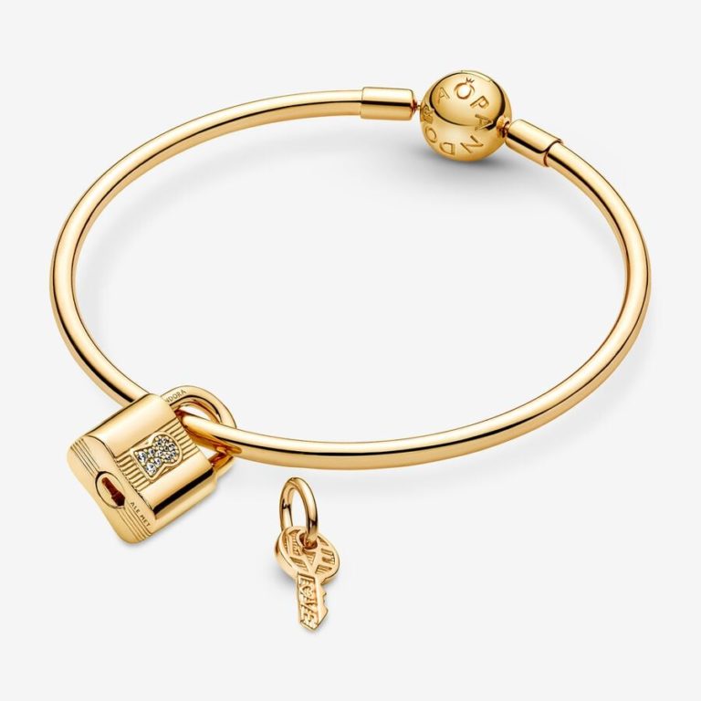 Gold bangle bracelet with a padlock charm and small key pendant on a white background.