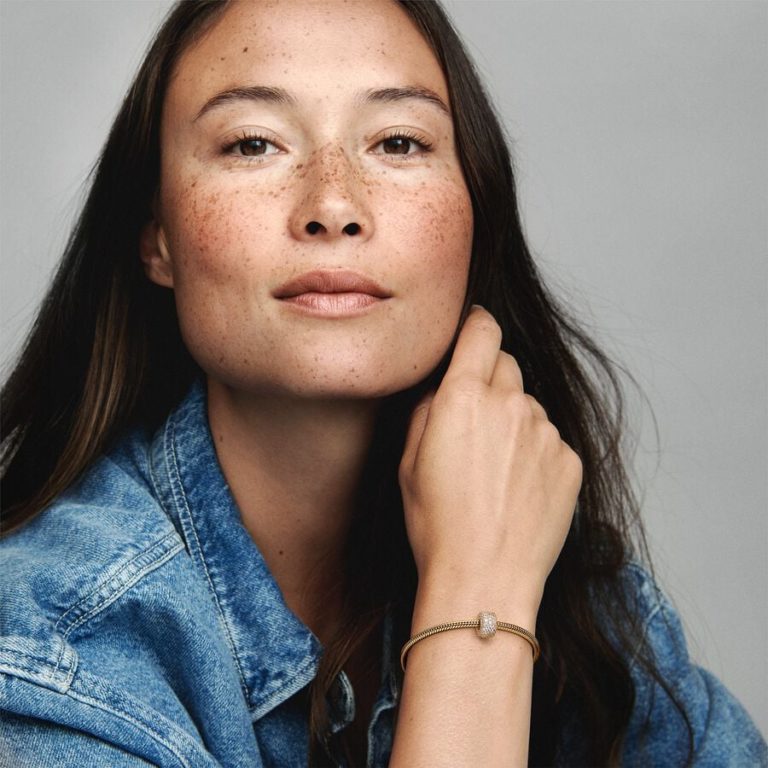 Person wearing a gold bracelet with a textured charm, shown in a close-up portrait.