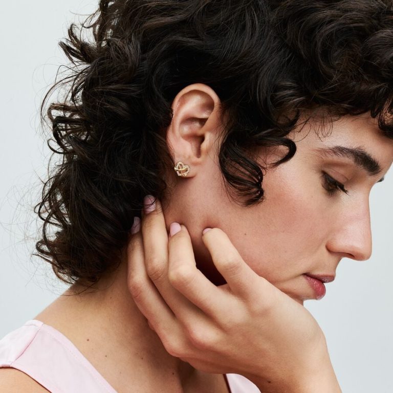 Person wearing a small gold heart-shaped stud earring with an infinity design.