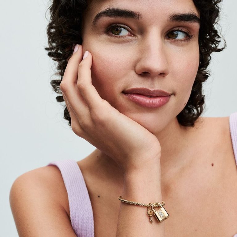 Person wearing a gold chain bracelet with a padlock charm and key pendant.